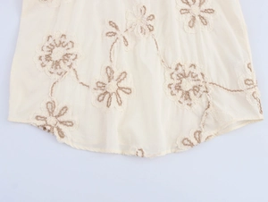 Detailed view of beige shirt featuring delicate flower embroidery and a rounded curved hem