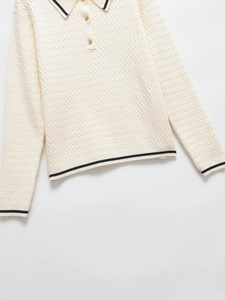 Close-up of knit polo shirt collar with black trim and gold buttons on cream fabric
