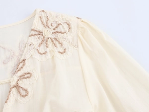 Detail showing 3D floral embroidery and lace stitching on a beige cotton dress
