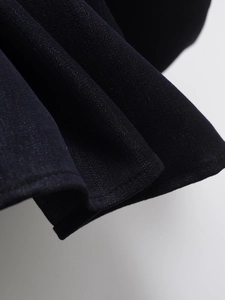 Detail of black woven denim dress showing pleated hemline and fine stitching craft