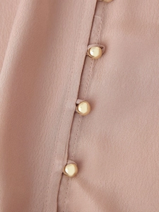 Macro detail of golden hemispherical buttons on dusty pink chiffon fabric blouse