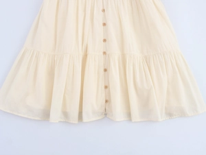 Detail of tiered ruffled hem on cream linen dress with wooden buttons and pleated texture