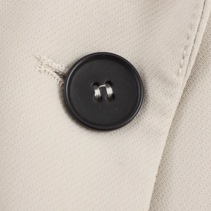 Close-up of a black four-hole button stitched on beige twill suit fabric texture