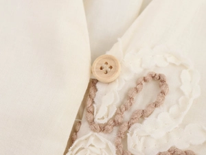 Macro detail of wooden button and intricate lace embroidery on beige linen dress fabric
