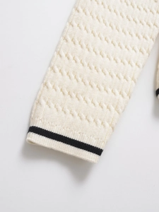 Detailed cable knit texture on cream sleeve with contrast black stripes at the cuff