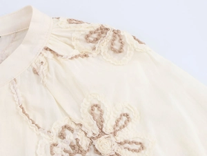 Detailed view of floral embroidery and ruffled stand-up collar on a beige blouse