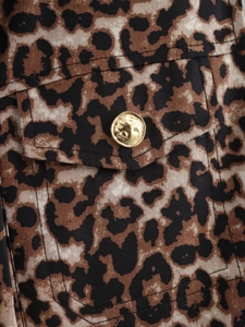 Macro view of leopard print fabric featuring a classic flap pocket and vintage gold button