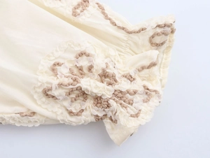 Detail of ruffled cuff with brown floral embroidery on ivory long-sleeve blouse