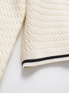 Detail view of cream knit sweater showing textured waffle pattern and black striped trim