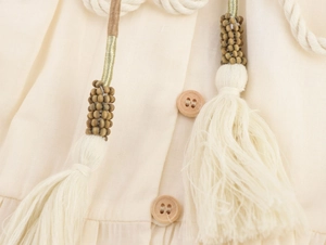 Macro detail of wooden buttons and woven drawstring with beaded tassels on beige dress