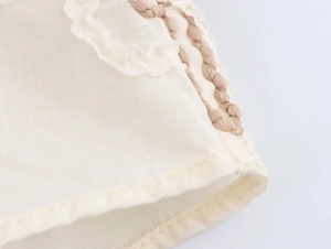 Detailed macro view of beige cotton linen fabric with brown floral embroidery and wavy edges