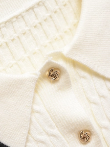 Detail of white knit polo sweater showing waffle texture and golden knot metal buttons