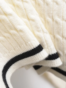 Detailed macro view of cable knit texture and contrast striped hem on this cream sweater