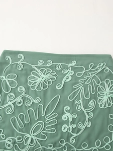 Dettaglio del tessuto verde salvia con intricato ricamo soutache floreale 3D sulla gonna