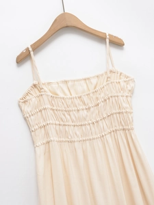 Detail of beige summer dress featuring adjustable straps and smocked bodice texture