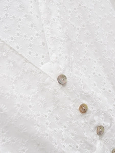 Gros plan détaillé de la robe blanche à col en V avec broderie marguerite et boutons en nacre