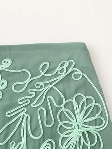 Primo piano dei ricami a cordoncino e motivi floreali su tessuto grigio-verde