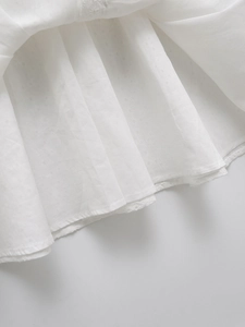 Détail de la robe blanche montrant la dentelle brodée et la texture du coton plissé