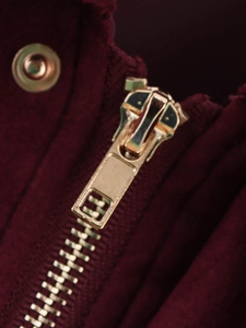 Macro detail of a high-quality gold metal zipper on dark burgundy corduroy jacket fabric
