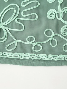 Dettaglio del ricamo floreale verde menta su tessuto crepe verde scuro con bordo a onde