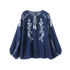Detail of white floral embroidery and tassel ties on a blue denim shirt for women
