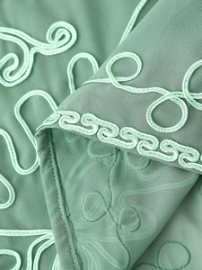 Dettaglio macro del tessuto verde menta con ricamo a cordoncino 3D e motivi floreali