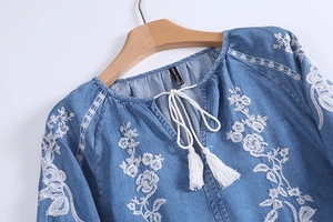 Detail view of light blue denim top with white floral embroidery and tassel drawstring