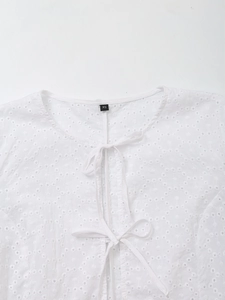 Detail of white hollow embroidery top with lace-up neckline and intricate pattern