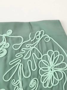 Dettaglio macro di ricamo floreale in cordoncino su tessuto verde salvia con trama 3D