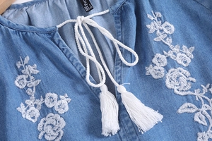 Close-up of V-neck denim shirt featuring white floral embroidery and tassel ties
