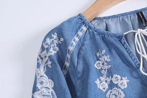 Detail of V-neck tie and white floral embroidery on a vintage blue denim shirt