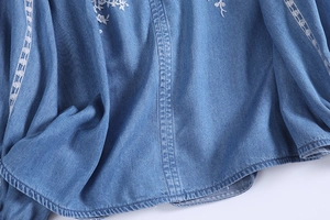 Detail of blue denim shirt featuring white floral embroidery and decorative stitching