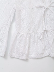 Detail view of white long sleeve top featuring delicate hollow embroidery and lace-up front
