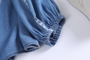 Detail of blue denim shirt sleeve featuring white floral embroidery and elastic cuffs