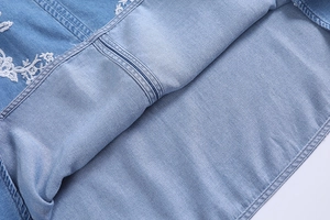 Detail shot of white floral embroidery on light blue denim fabric texture and hem