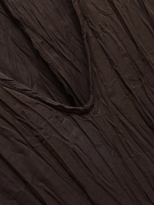 Macro detail of V-neckline on dark brown pleated dress showing textured fabric and stitching