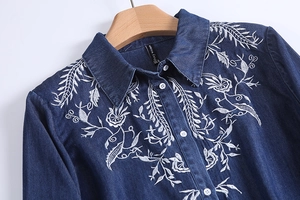 Detail shot of white floral embroidery on premium dark blue denim long sleeve shirt