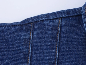 Detailed close-up of dark blue denim fabric texture with orange double stitching details