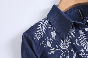 Close-up of white floral embroidery on dark blue denim shirt with white buttons