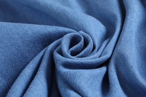 Macro shot of soft blue denim fabric texture showing detailed fiber weave and pleats