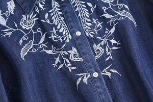 Detail of white floral embroidery on premium dark blue denim shirt with white buttons