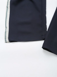 Detailed view of dark blue trousers with side cream stripes and green piping decoration