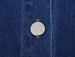 Detail of blue denim fabric with vintage silver button and orange contrast stitching