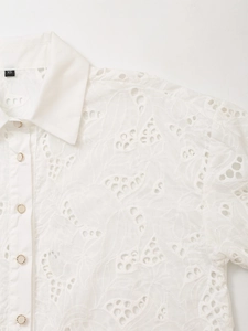Detailed view of floral hollow embroidery and gold-rimmed buttons on white shirt