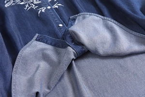 Detailed close-up of white floral embroidery and button closure on dark blue denim shirt
