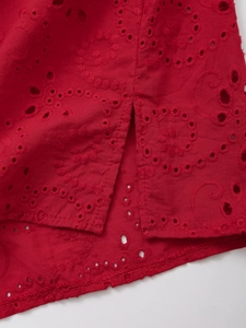 Detailed close-up of red cotton shirt with eyelet embroidery and side slit hem