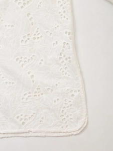Close-up of intricate floral embroidery and broderie anglaise hollow-out detail on white fabric