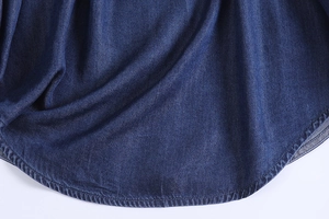 Detailed view of the dark blue denim shirt's rounded hem with high-quality stitching