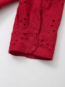 Detail of red shirt cuff with intricate eyelet embroidery and matching round buttons