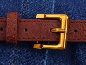 Close-up of a brown textured leather belt with a vintage gold square buckle on denim